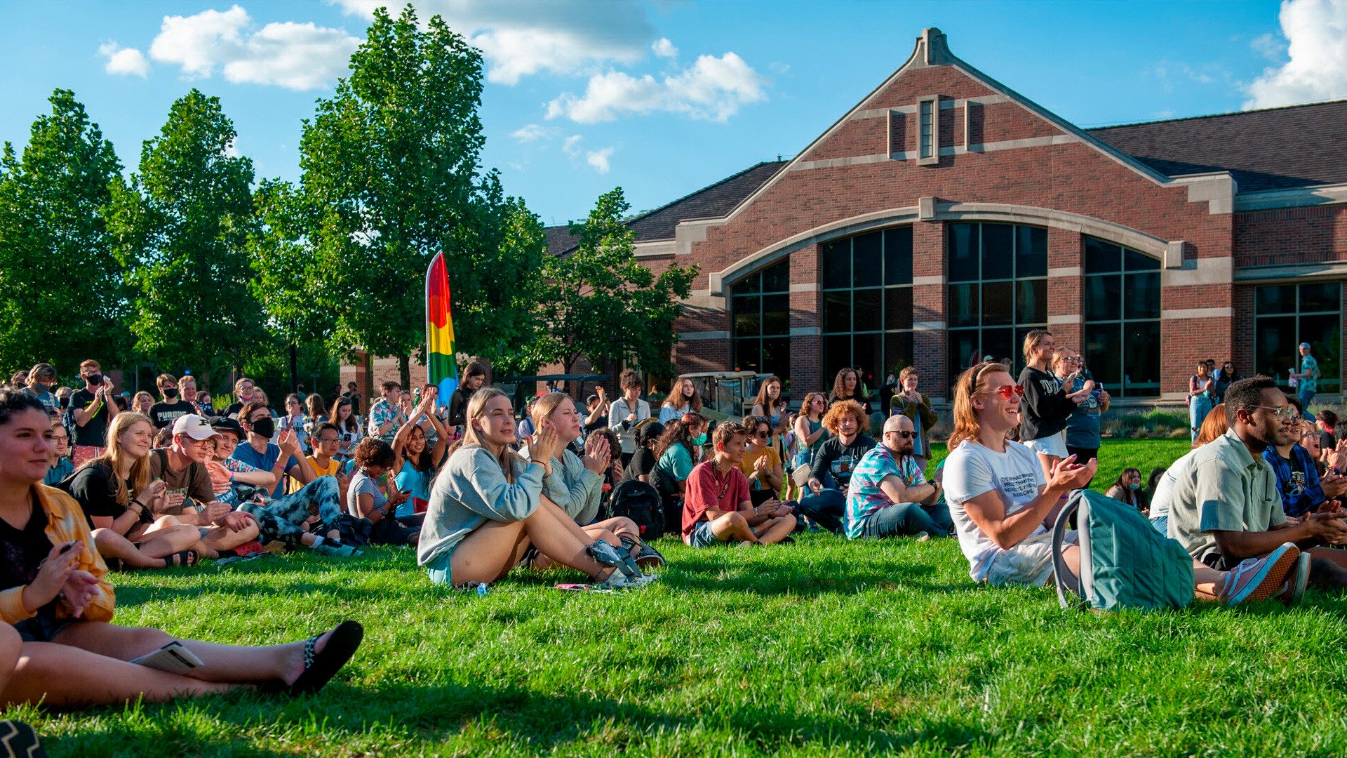 LGBTQ Callout crowd of students sitting in the grass in the green space near Wiley Dining Court.