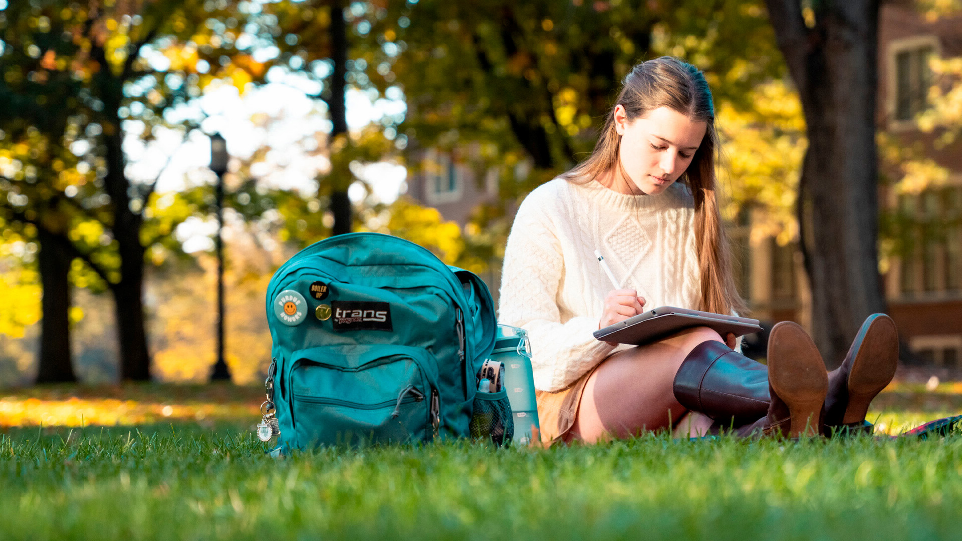 Female student studying on an iPad while sitting in the grass on Purdue's campus. 