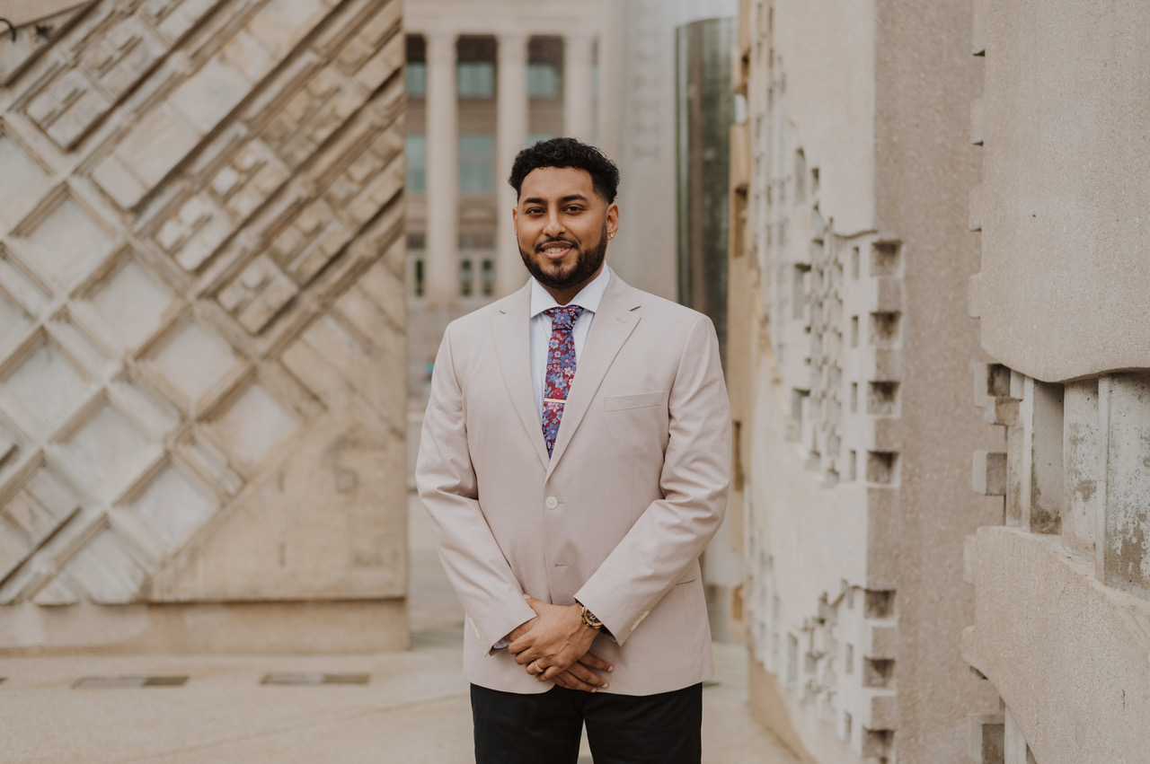 Roneil Kumar standing in front of a tan background.