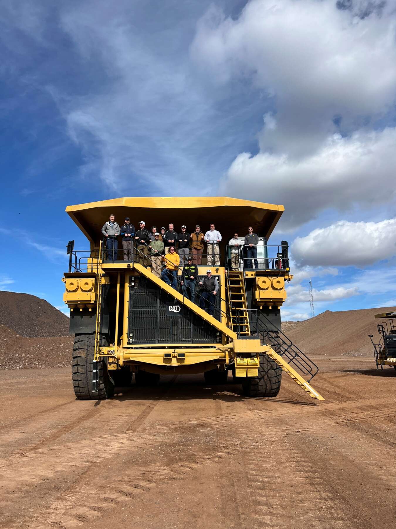 Representative from Purdue stand on a Caterpillar mining truck positioned in the Arizona desert. The sky is blue and the group is smiling.