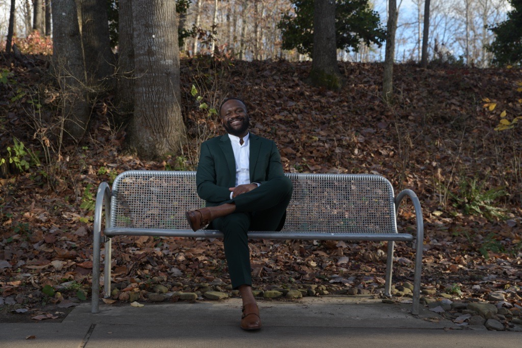 Tomy Mukendi sitting on a bench outside on a cool, crisp fall day.