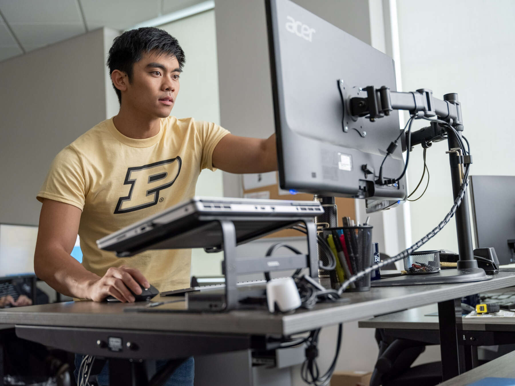 A man wearing a Purdue shirt works on a desktop computer