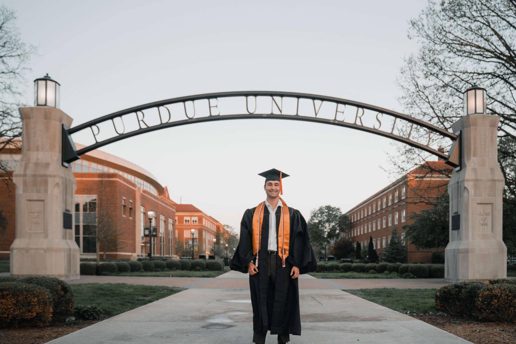 Ayrton Birnbaum in graduation robes, posing in front of the Purdue arch.