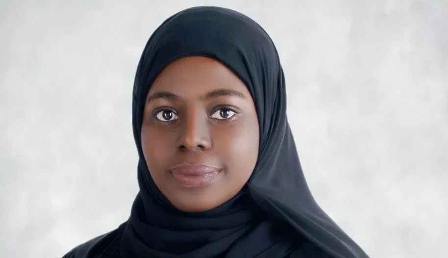 Moza posing against a black background. She is wearing a black dress and black hijab.