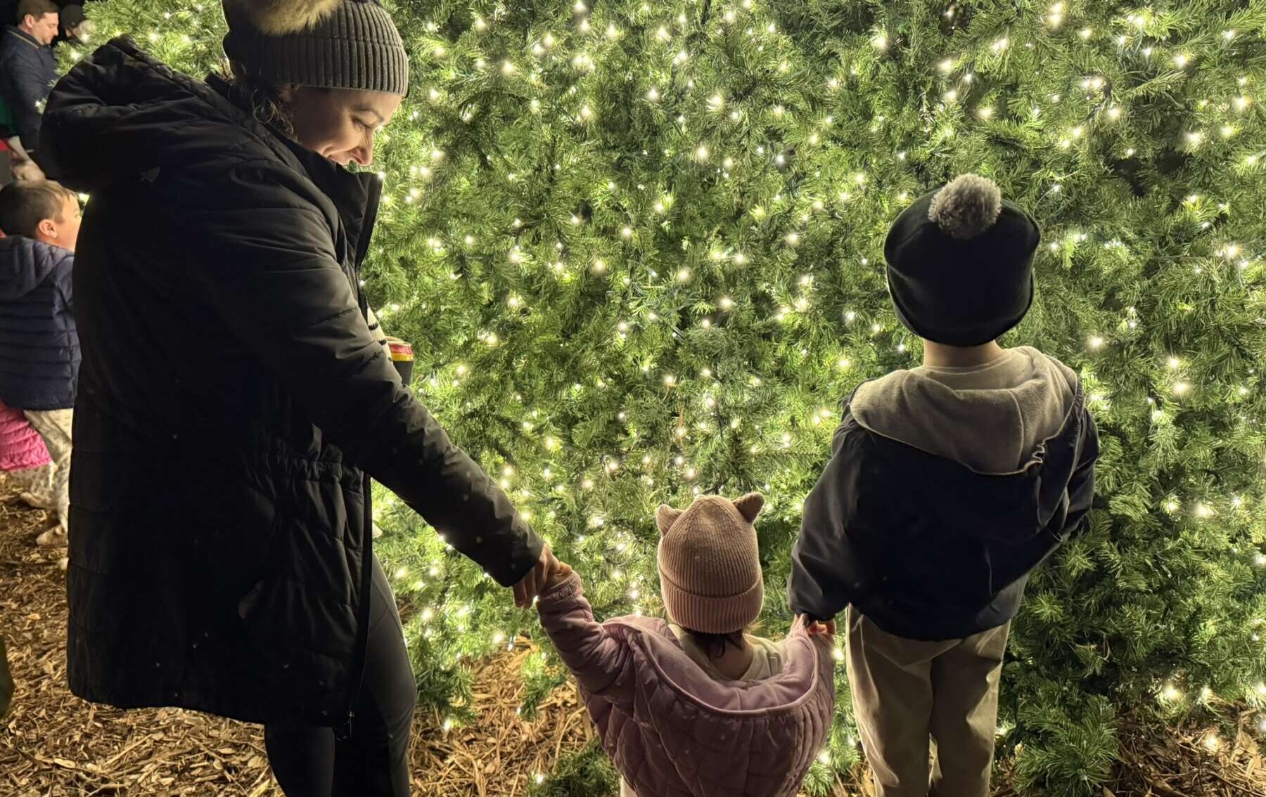 Jacob Luna's wife and two young children stand in front of a large Christmas tree wearing winter clothes.
