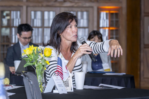 Julie Felgar, vice president for government affairs and defense at JetZero. Julie Felgar asks a question with a microphone in her hand. She is wearing a white and black striped shirt.