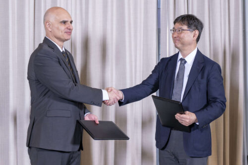 Senior Vice President for Partnerships and Online Dimitrios Peroulis with Naoyuki Maekawa, director and general of the Innovation Department at JETRO. Dimitrios Peroulis and Naoyuki Maekawa shake hands. Both men are wearing suits and holding black folders.