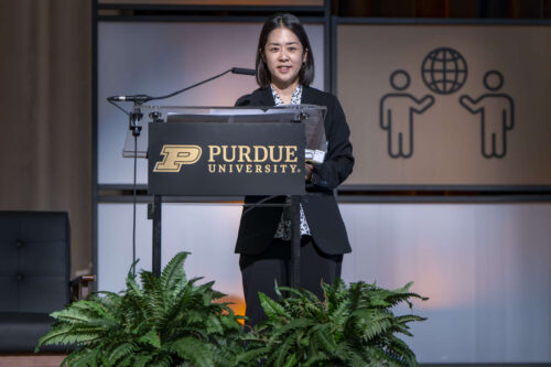 Keynote speaker Yuka Suzuki, counselor of the Embassy of Japan in the U.S. Yuka Suzuki addresses a crowd behind a podium. She is wearing a black blazer and a white shirt with a floral pattern.