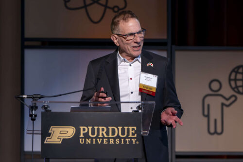 Rick Gottscho, president of SemiSan, LLC. Rick Gottscho addresses a crowd at Purdue University. He is wearing a black blazer and white dress shirt.