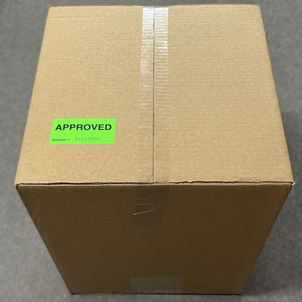 A sealed cardboard box with a bright green label on top that reads “APPROVED.” The label also lists a request number.