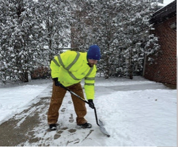 A Building Services employee clearing walkways in front of a campus building.