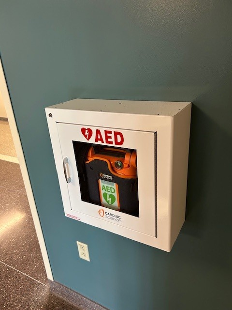 AED located in the main corridor of DLR near the stairs across from the north exterior entrance.