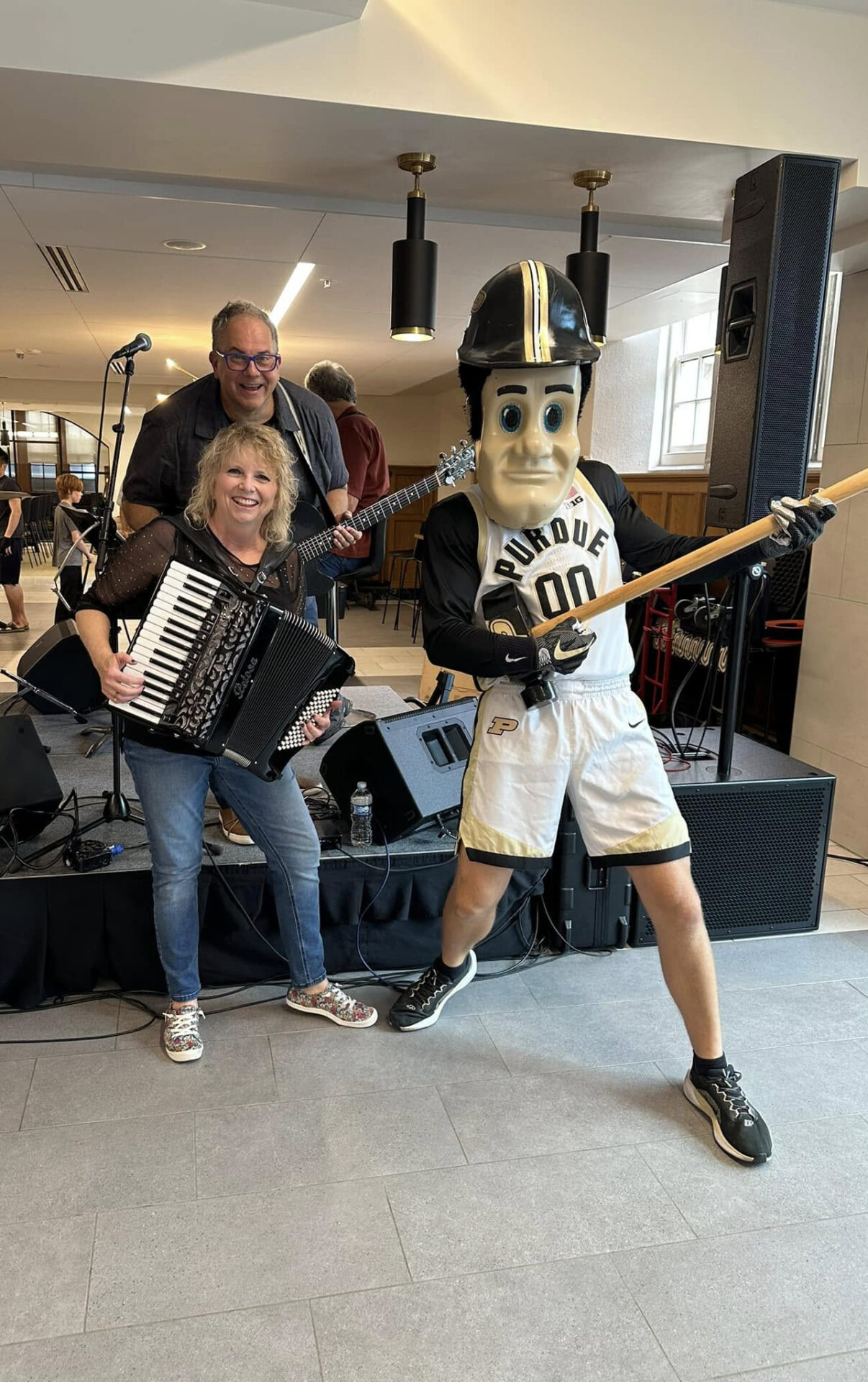 Band members at Summer concert Series posing and smiling with Purdue Pete inside next to the Ever True Stage.