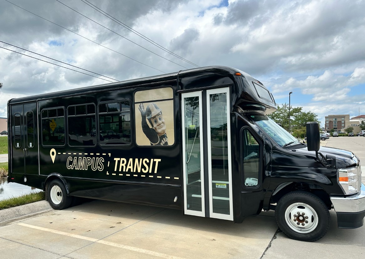 The Campus Transit on demand shuttle. A black shuttle bus with the Purdue Campus Transit logo on the side, and an image of Purdue Pete waving in the front window.
