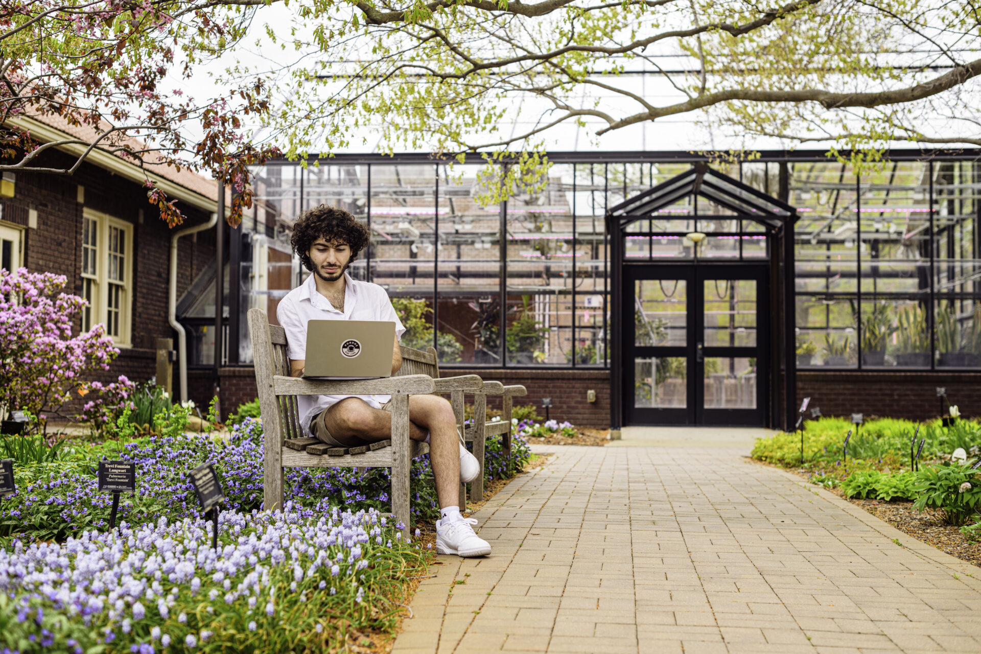 Student sitting on a bench with a laptop in the Purdue Horticulture Park