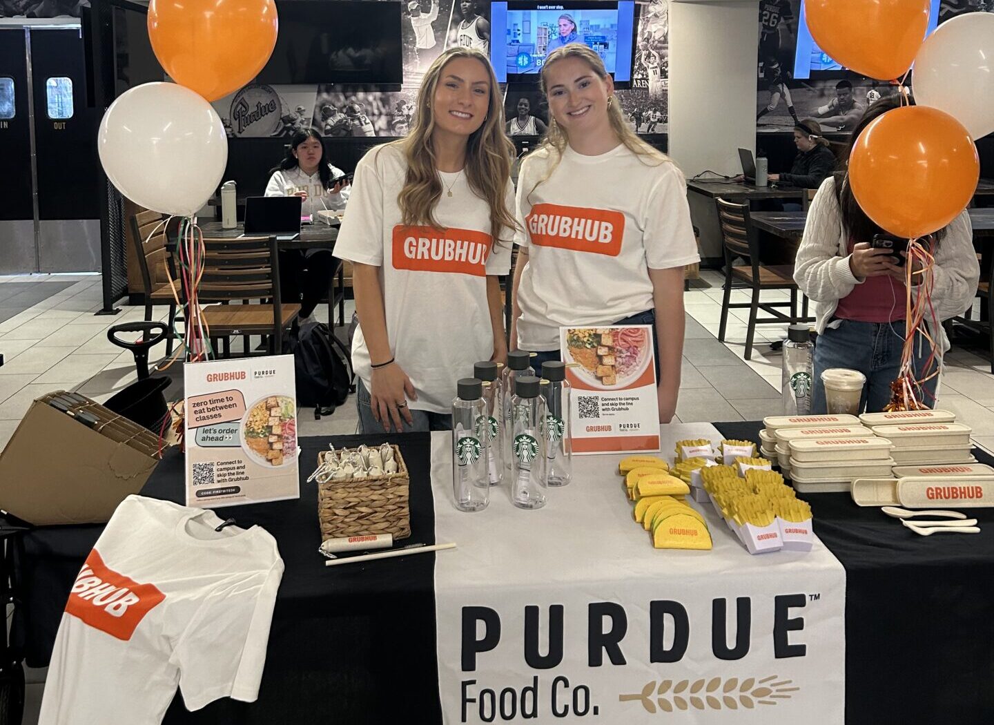 Purdue Food Co. employees tabling for Grub Hub with giveaways on table in front of them.