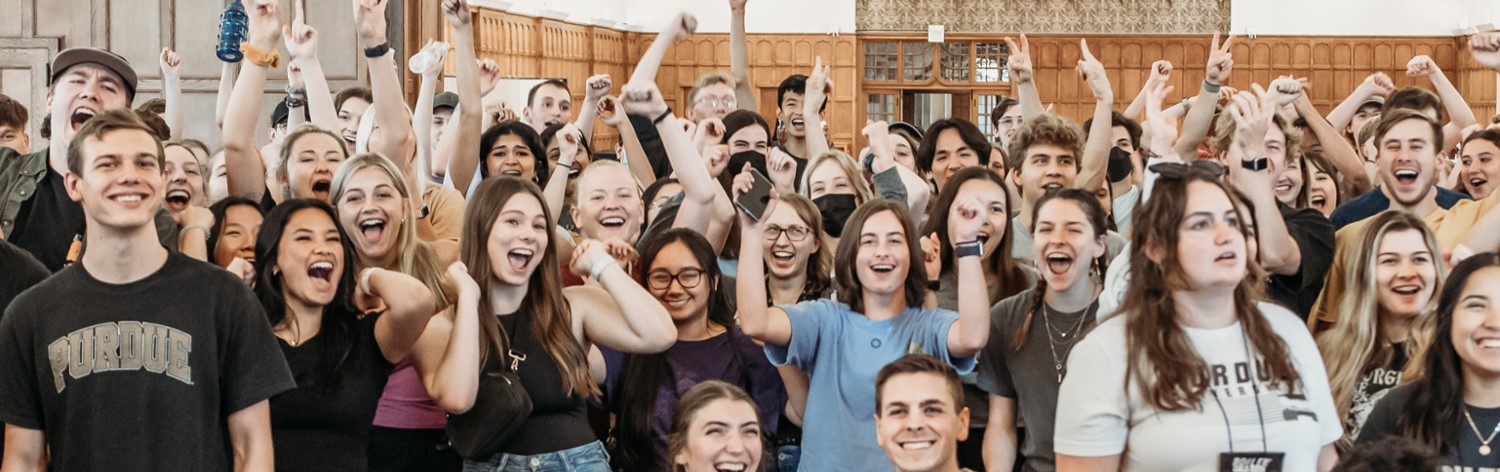 pictured: large group of students stand and cheer during a summer visit day activity