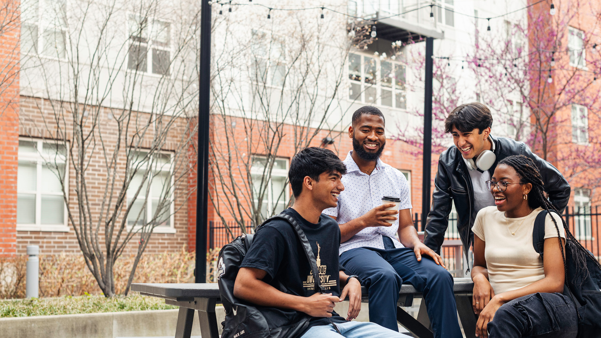 A group of students sitting at an outdoor bench while talking and laughing.