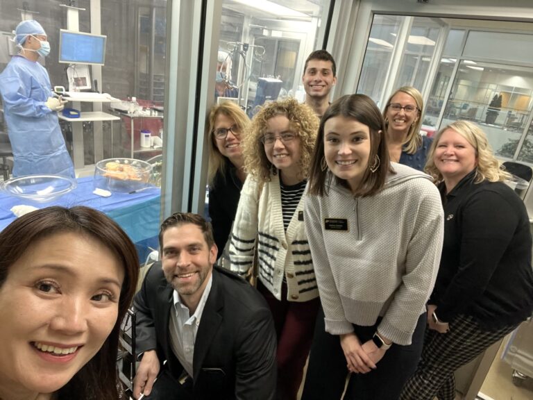 Group of people smiling while observing a medical simulation lab.