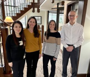 Four professionals posing for a photo together in an indoor hallway near a wooden staircase.