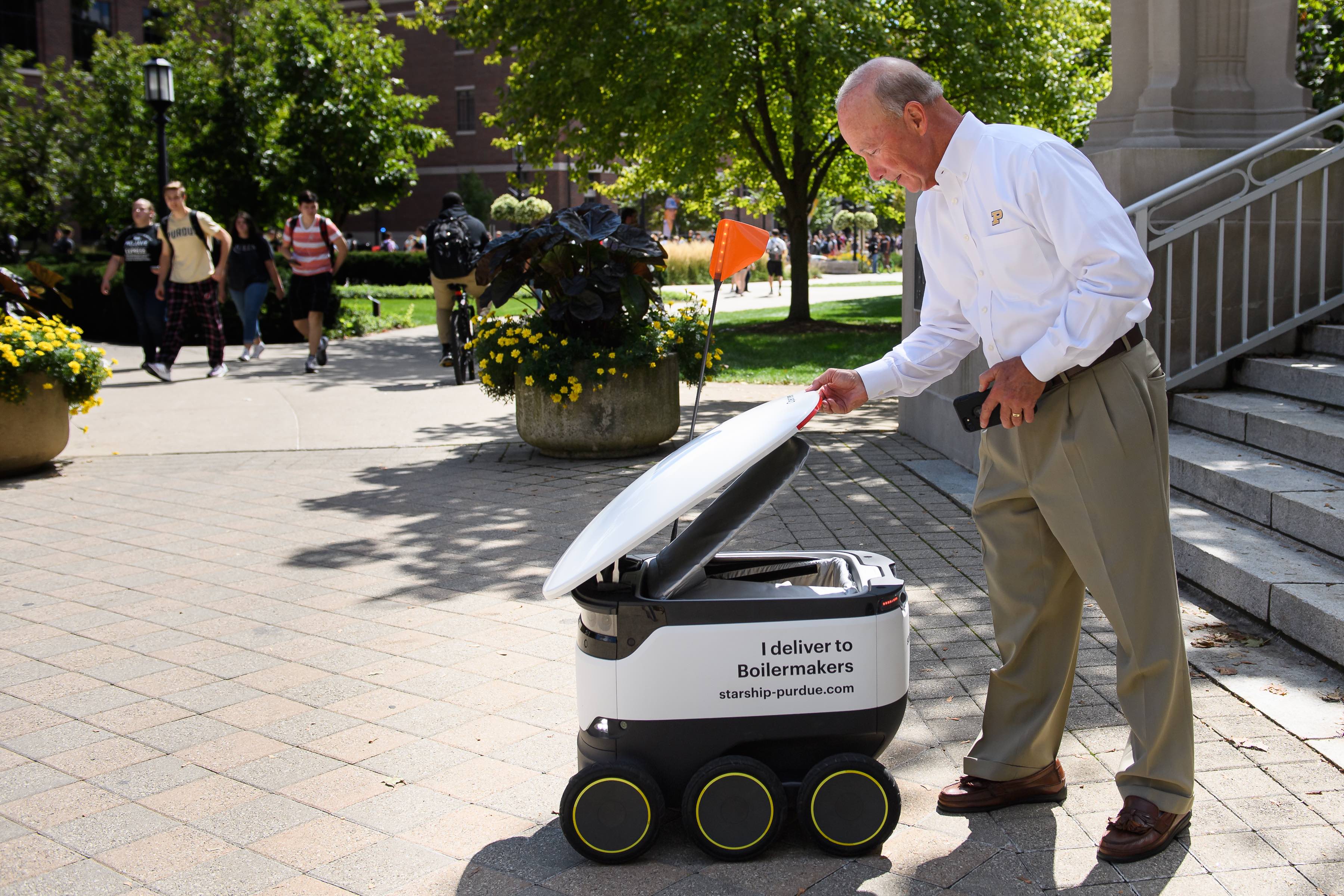 Purdue President Mitch Daniels greets a Starship delivery robot