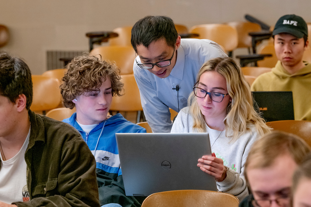 Pictured: Students in a classroom work closely with their professor, all of them on laptops.