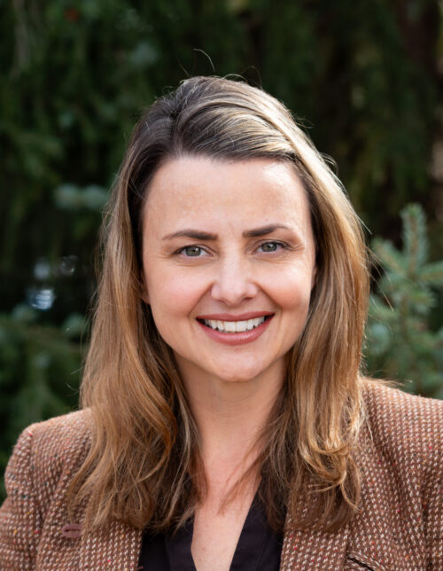 Headshot of a person wearing a brown jacket and a black shirt
