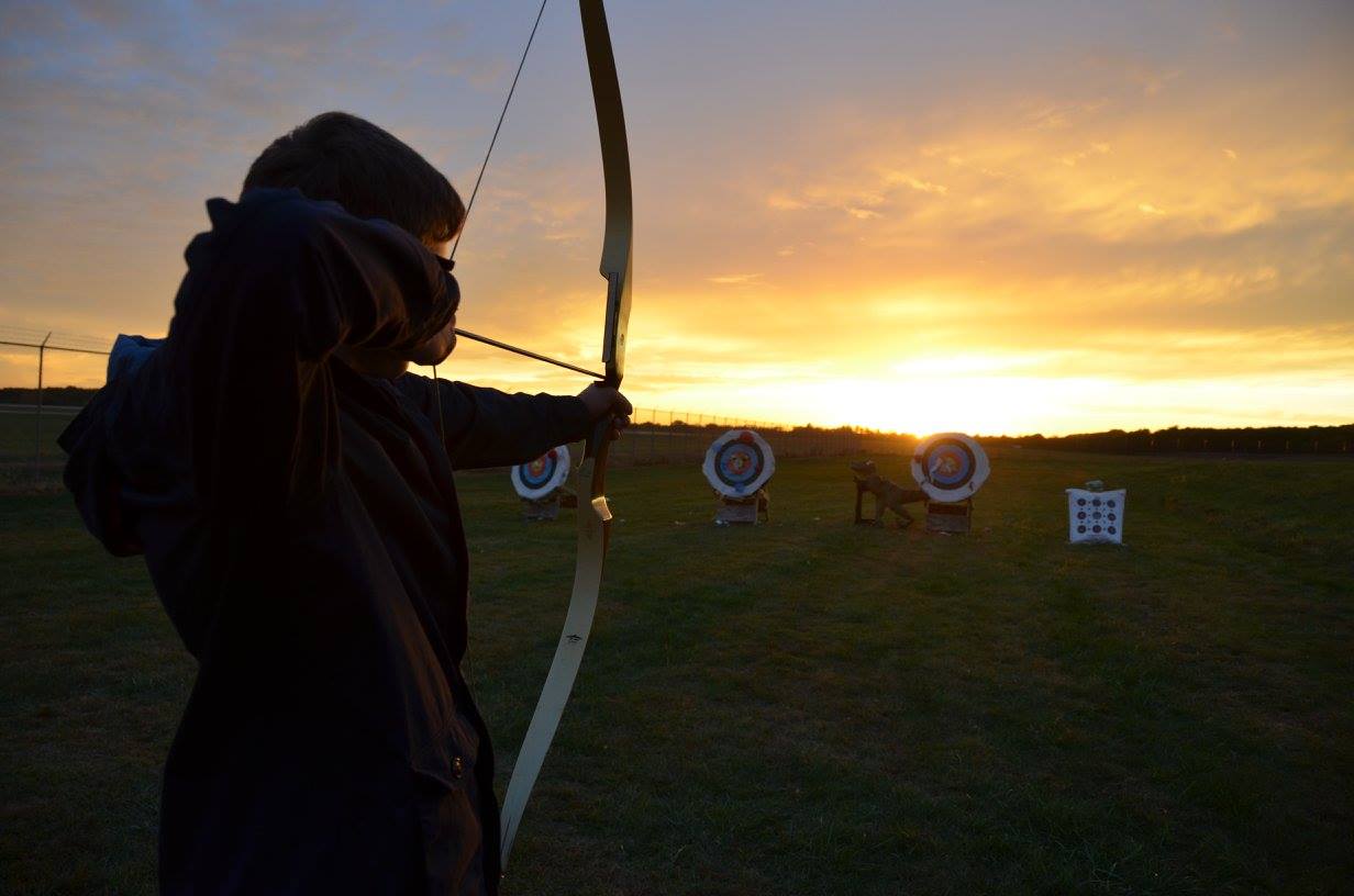 Person shooting a bow and arrow with a sun set behind them