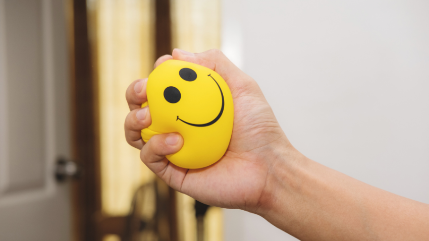 Someone squeezing a stress ball with a yellow smiley face on it