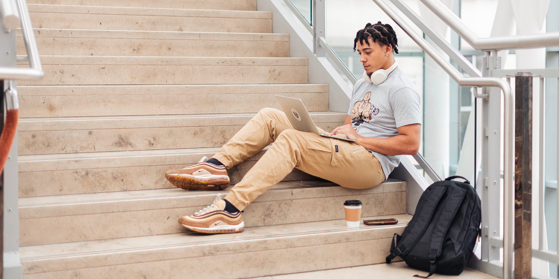 Male student sitting on steps with laptop and bookbag
