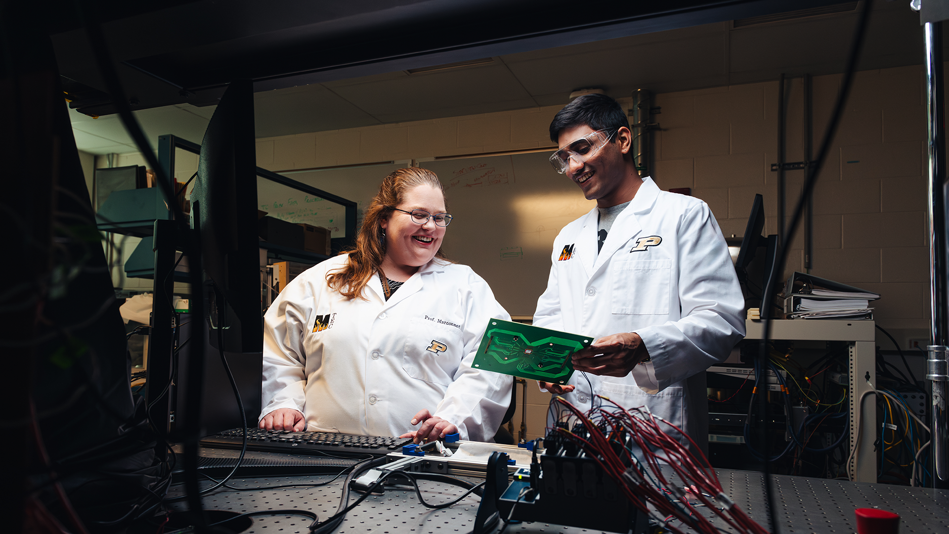 Two students wearing lab coats looking at microchip technology