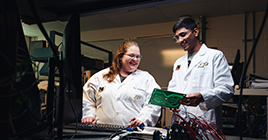Two students wearing lab coats looking at microchip technology
