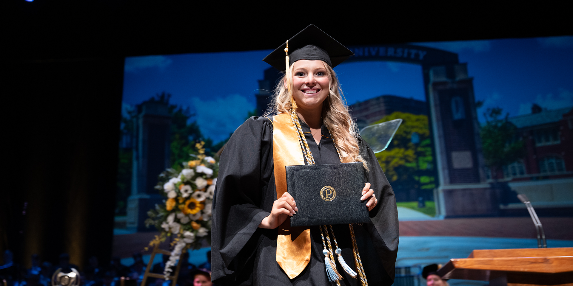 Graduate holds her diploma and poses for photo on the stage during commencement.