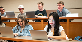 Students looking at laptops in a classroom with stadium seating
