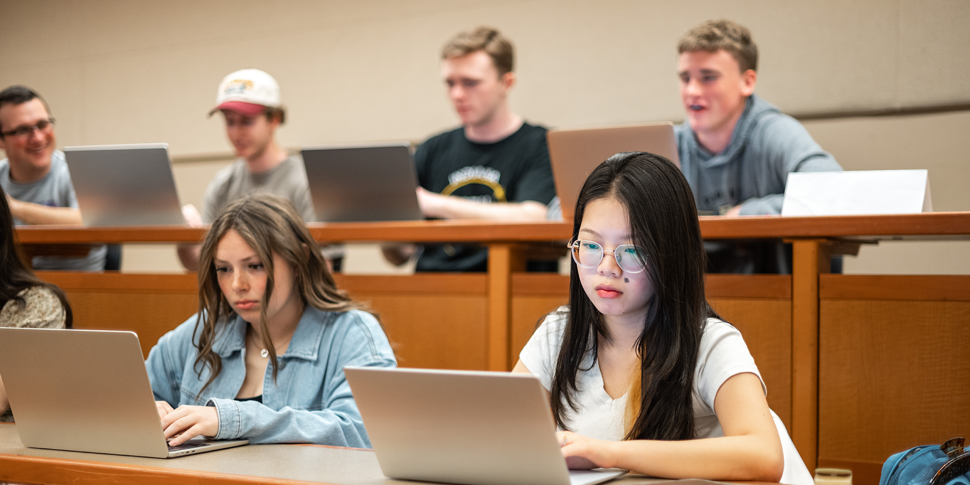 Students looking at laptops in a classroom with stadium seating