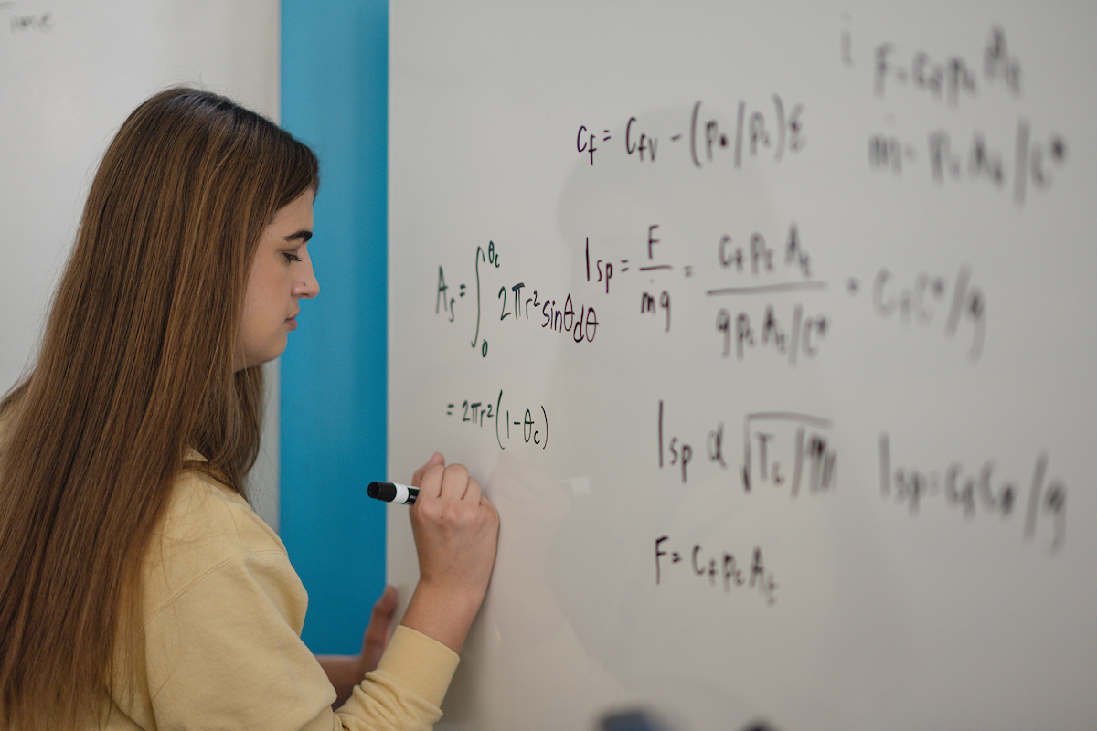student completing a long-form math problem on the white board
