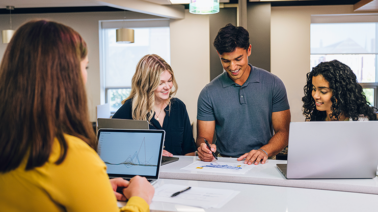 Students gathered around an assignment while one student takes notes.