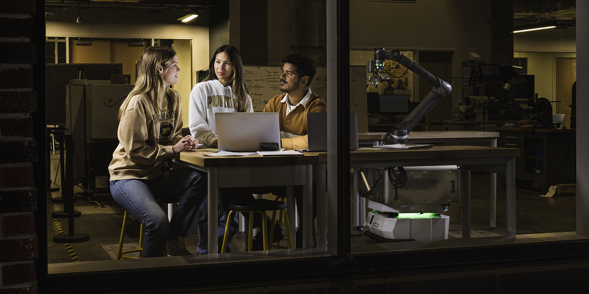 Looking in through a window at three students studying together at a workstation.