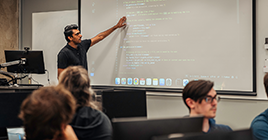 Instructor pointing to a screen in front of a classroom of students