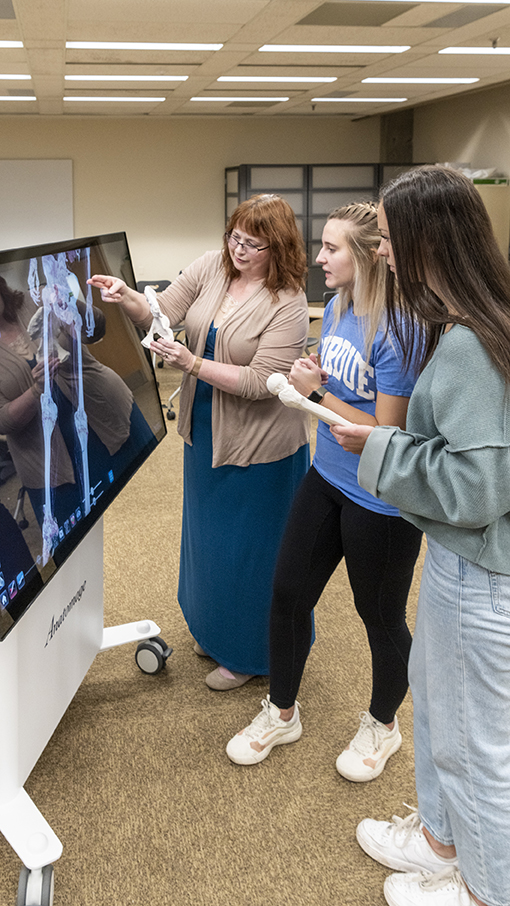 An instructor demonstrates anatomy holding skeletal bone pointing to the anatomage table