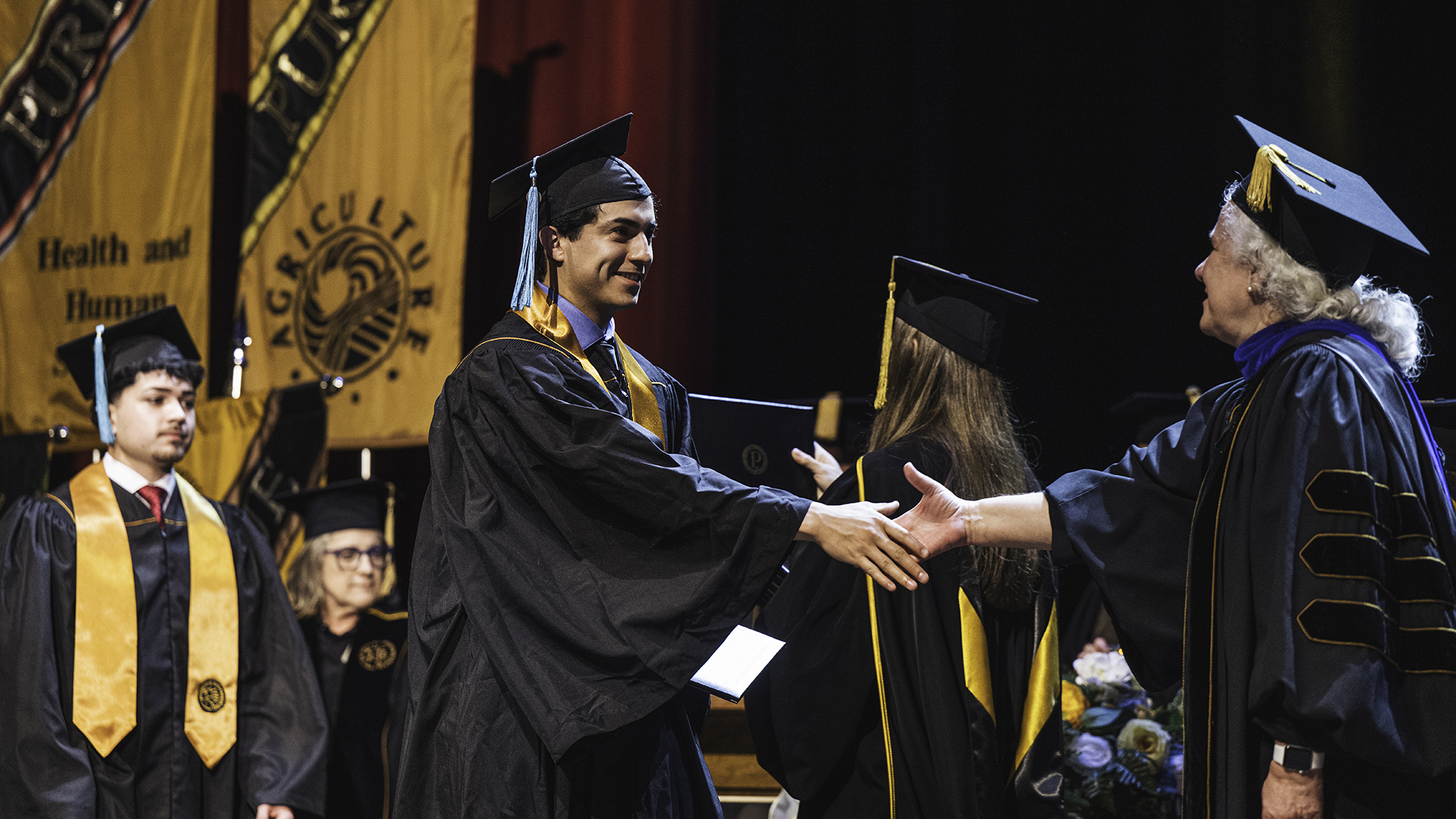 A graduate shakes hands with his college's administrator as he crosses the stage during commencement.