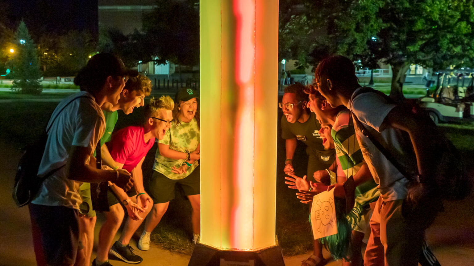 Image showing students gathered around large colorful glowing pole, excitedly yelling