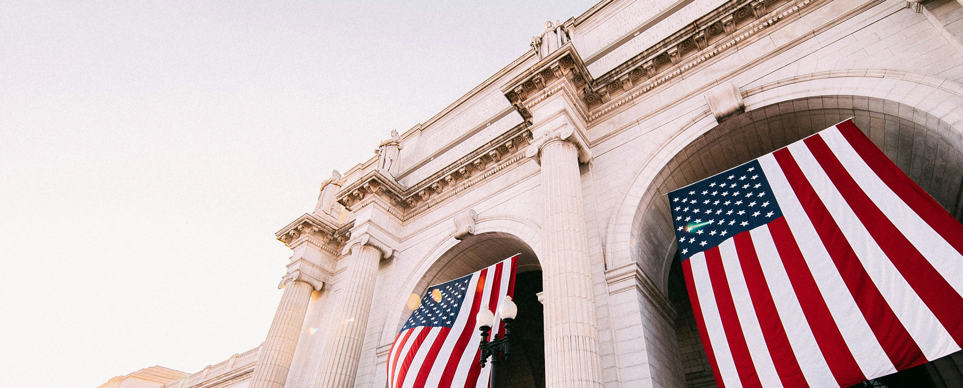 Flags for the United States of America hanging from archways of a government building.