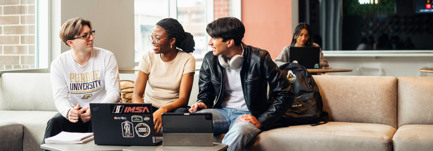 A group of three students sitting in front of a laptop having a conversation.