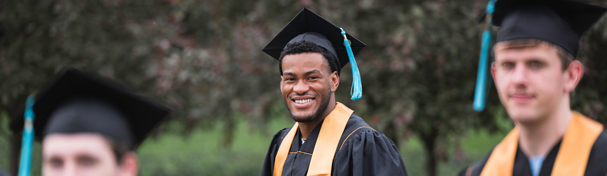 A young man at graduation smiling at the camera with other graduates around him.