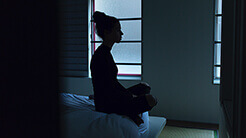 woman seated on bed in darkened room
