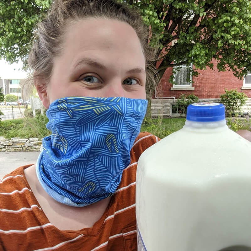 Person outdoors in mask, holding gallon jug of milk
