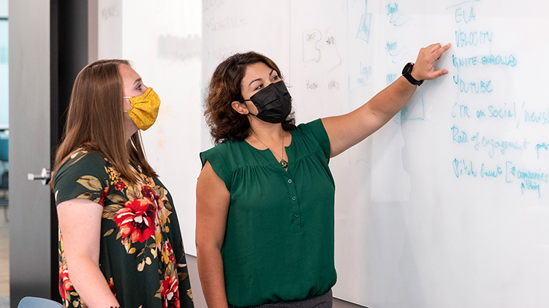 Two women talking by white board