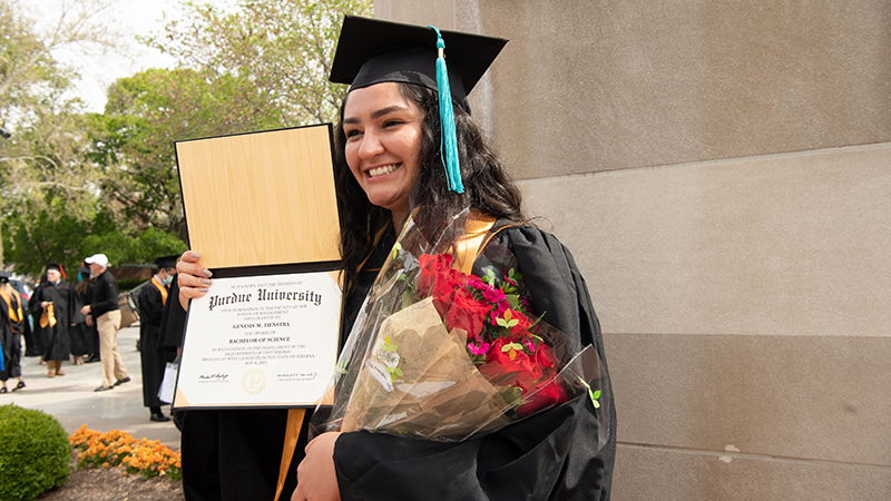 grad with diploma, flowers on campus