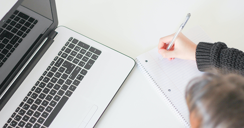 writing in notebook next to laptop